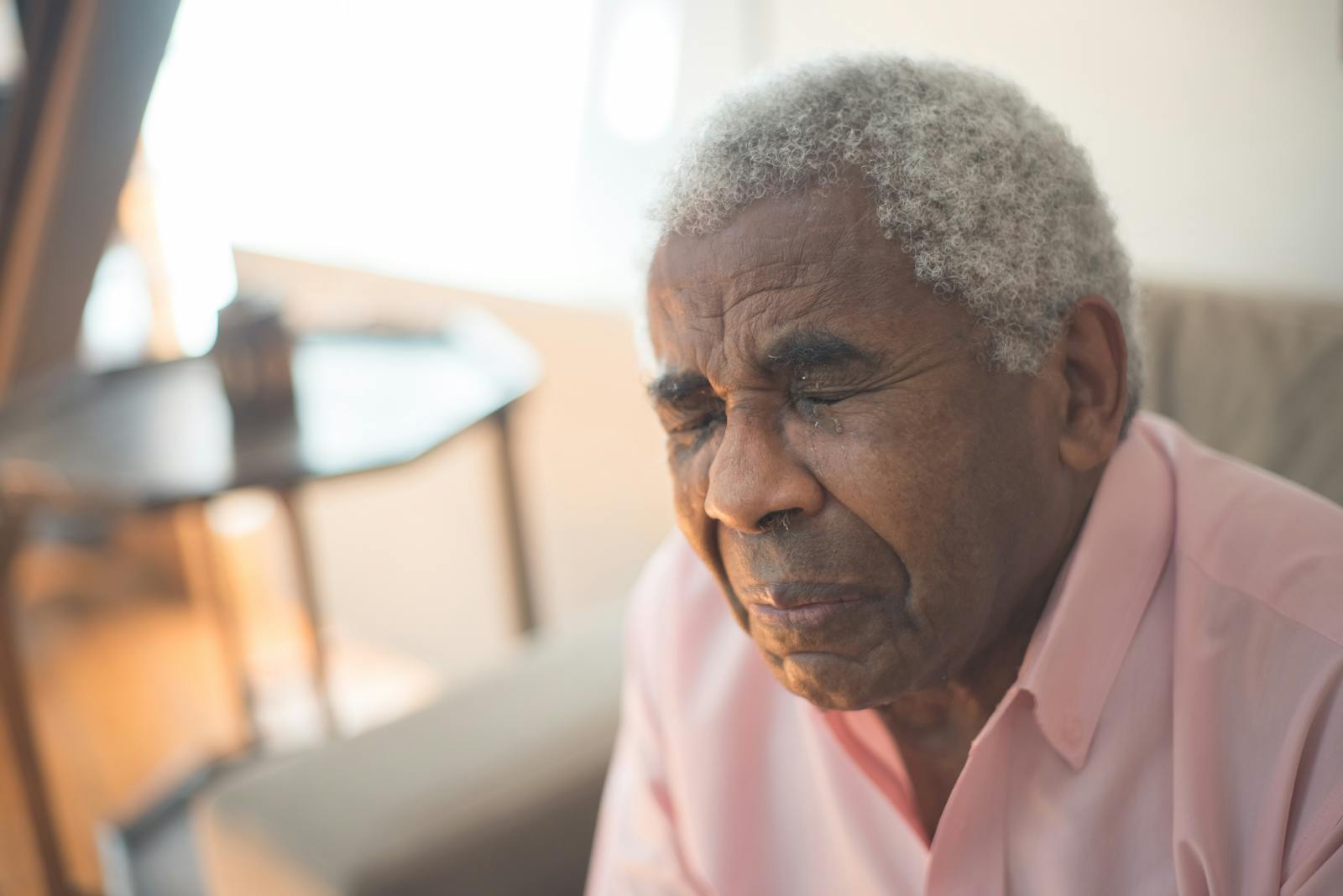 An elderly man with gray hair expresses deep emotion, sitting indoors in a moment of grief.